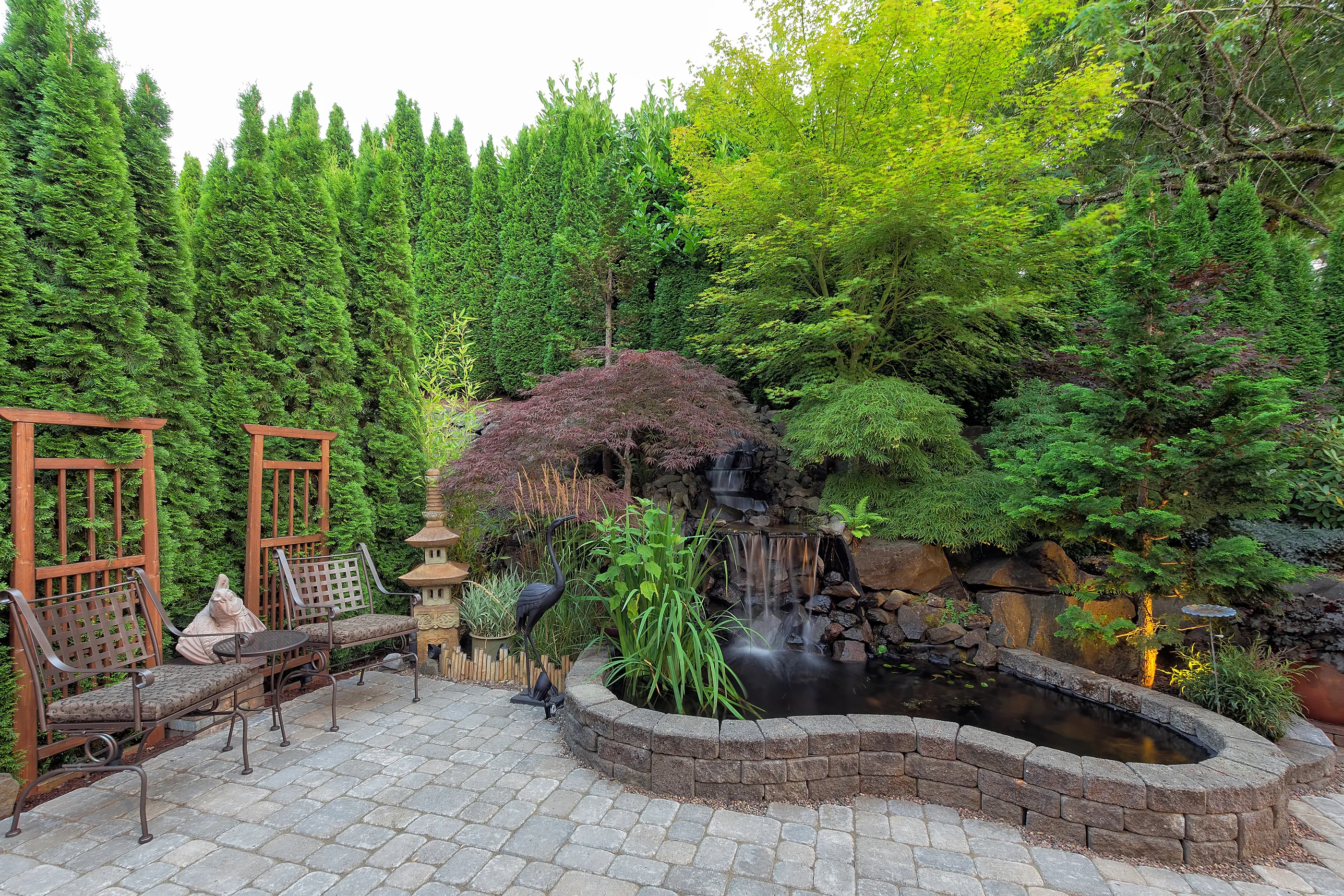 Paver patio with a stone-edged pond surrounded by mature evergreen planting