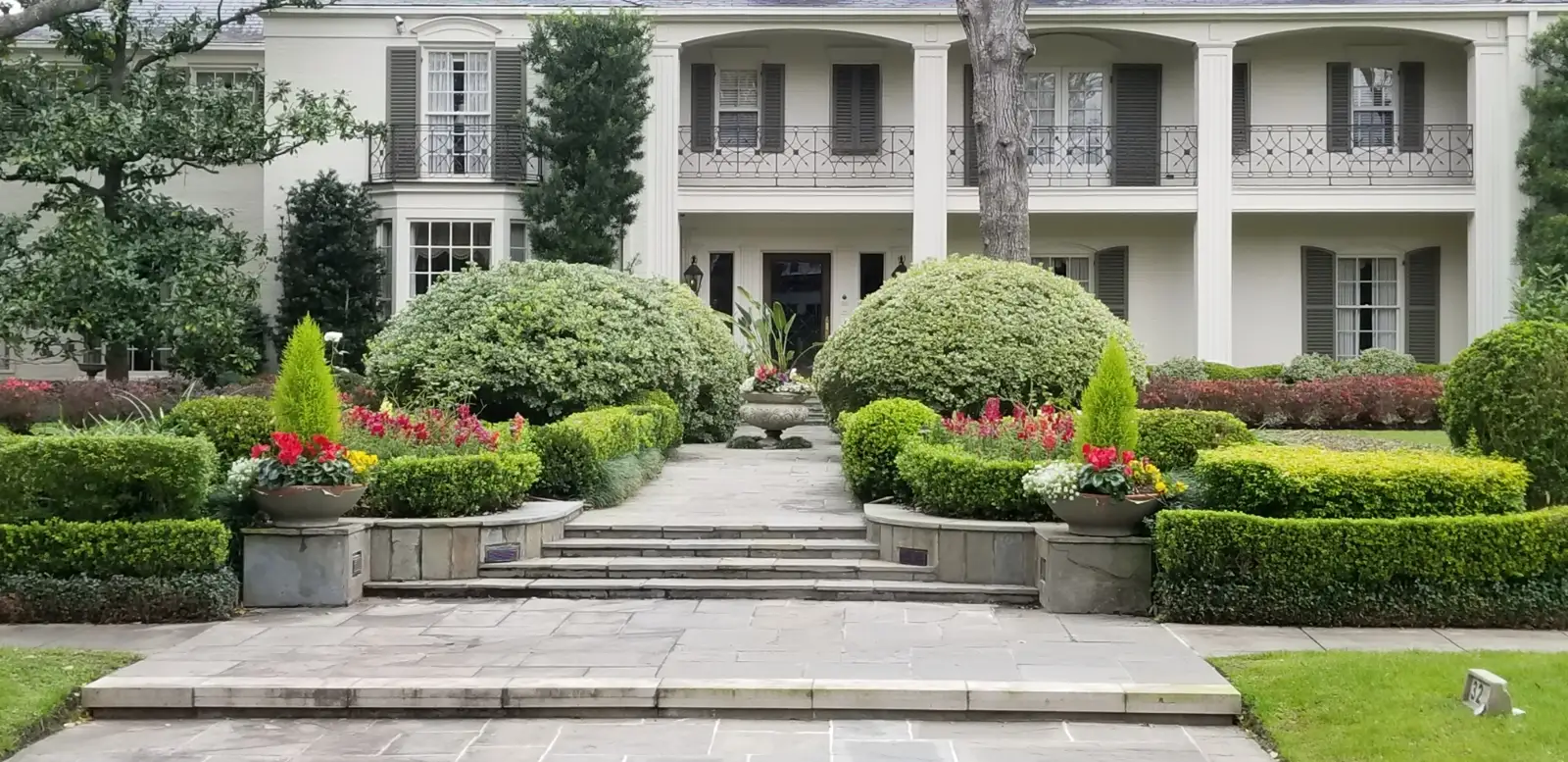 Formal front garden with flagstone steps, clipped boxwood hedges and flowering urns