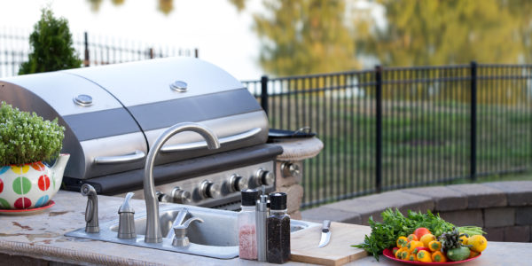 Preparing a healthy summer meal in an outdoor kitchen with gas barbecue and sink on a brick patio overlooking a tranquil lake with tree reflections